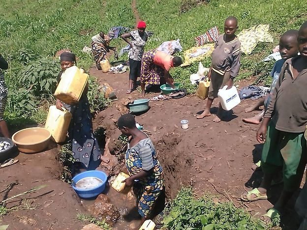 Families collecting water from an unprotected source in North Kivu, DR Congo