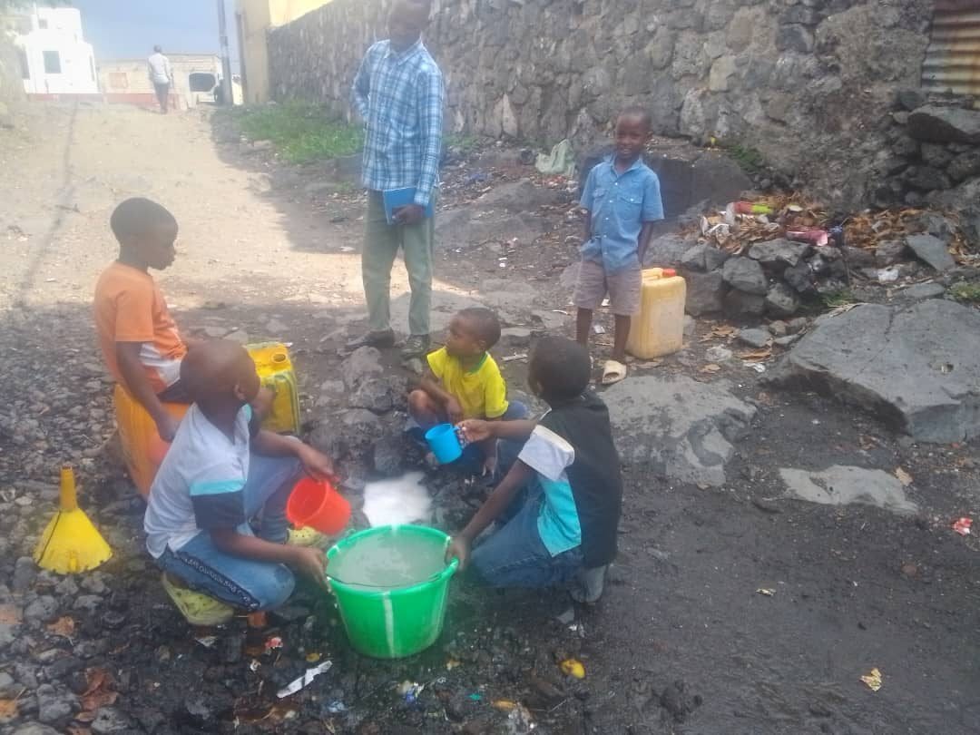 Children filling basins and jerrycans from a pool on volcanic rock in Goma, DR Congo