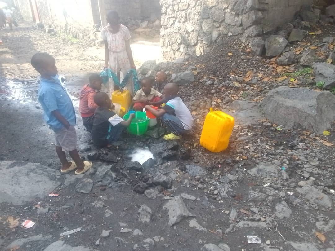 Children filling jerrycans from water pooled between volcanic rocks in Goma, DR Congo
